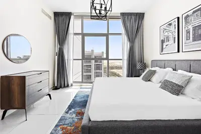 a white bedroom with a large bed and a large window at VayK - Great 1BR Apartment in Damac Hills in Dubai