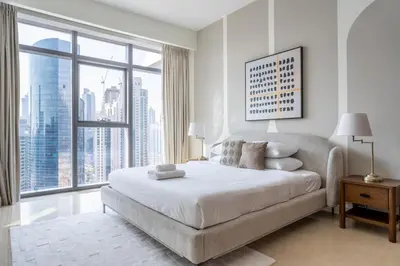 a white bedroom with a bed and a large window at GuestReady - 2BR City View | Canal | High Floor in Dubai
