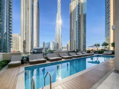 a swimming pool with lounge chairs and a city skyline at Direct Burj & Fountain Views - Designer 4BR Haven! in Dubai