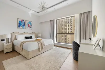 a white bedroom with a bed and a large window at 2BR Marina View Steps from the Beach in Dubai