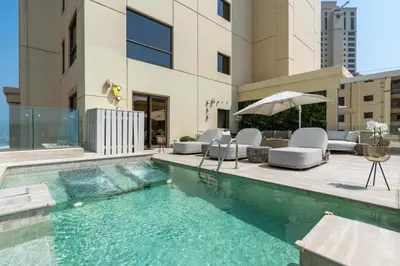 a swimming pool with chairs and an umbrella next to a building at Stunning VIP Penthouse JBR cinema&spa&pool in Dubai