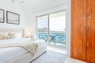 a white bedroom with a large bed and a balcony at Lake-View Apartment Near City Centre Meaisem Mall, Just Minutes from Dubai Autodrome and ICC Cricket Stadium - The Crescent A, Dubai Production City by Deluxe Holiday Homes in Dubai