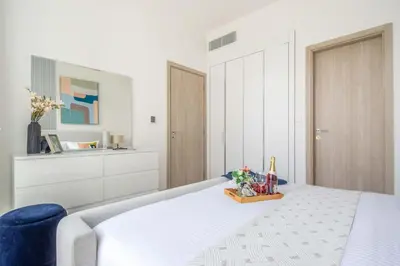 a white bedroom with a bed and a blue chair at Frank Porter - Luma22 West Tower in Dubai