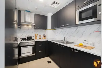 a kitchen with black cabinets and a sink and a microwave at Vogue JVC Jeewar Tower near Circle Mall, One Bedroom Apartment with Balcony and Park view, Access to all Amenities in Dubai