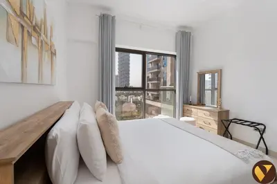 a white bedroom with a large bed and a window at Vogue JVC Jeewar Tower near Circle Mall, One Bedroom Apartment with Balcony and Park view, Access to all Amenities in Dubai