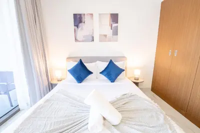 a bedroom with a white bed with blue pillows at EasyGo - Chic Studio Escape in Dubai Sports City in Dubai