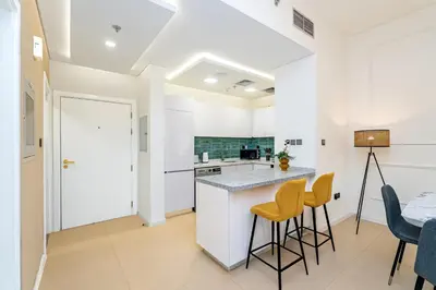 a kitchen with white cabinets and bar stools at Escape24 Chic 1BR in Al Furjan near Metro in Dubai