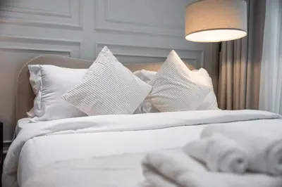 a white bed with white pillows and a lamp at Brand New Luxury Studio, Amazing Pool & Gym in Dubai