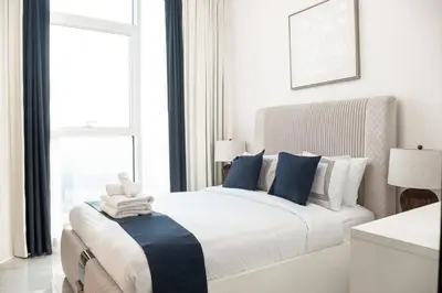 a white bedroom with a large bed with blue pillows at Gemz by Danube, Private Pool, Al Furjan - Onelink in Dubai