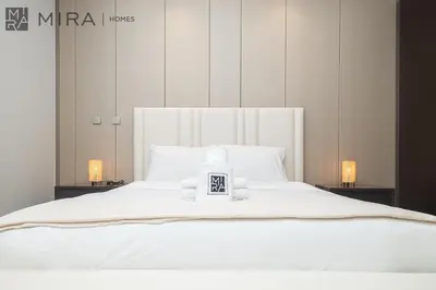 a white bed with a clock on top of it at Mira Holiday Homes - High View 2 Bed Oasis at Nobles Tower with Sauna in Dubai