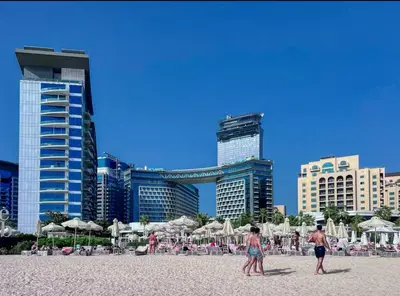 a group of people walking on a beach with buildings at Séjour raffiné et inoubliable in Dubai