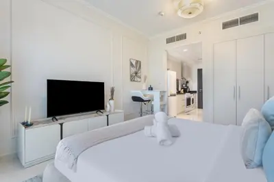a white bedroom with a large bed with a flat screen tv at Sky-High Luxury Studio Overlooking Trump Golf Club-Carson A, DAMAC Hills, Dubai in Dubai