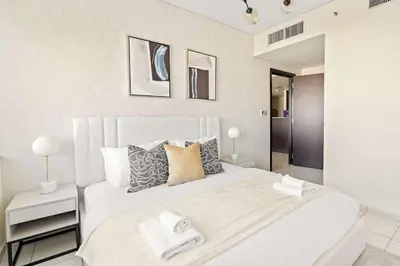 a white bedroom with a large white bed with two towels at Silkhaus Deluxe 1BR Stay in Sky gardens in DIFC in Dubai