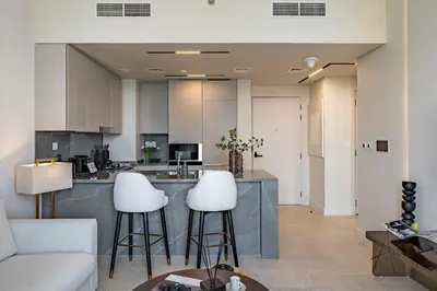 a living room with a kitchen with white stools at Burj Khalifa View Luxe 1BR Paragon by IGO in Dubai