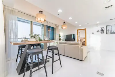 a kitchen and living room with a table and stools at 3BR with Sea View, Short Stroll From Marina Walk and JBR Beach, With Easy Access to Tram and Metro - Ocean Heights, Dubai Marina by Deluxe Holiday Homes in Dubai