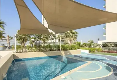 a swimming pool with an umbrella over a building at Brand New 1BR - Infinity Pool & Golf Views in Dubai