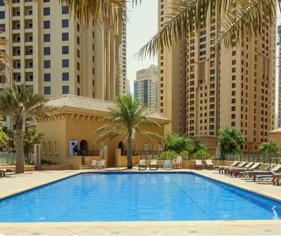 a large swimming pool with palm trees and buildings at Lux 4BR JBR I Sea View I Walk to Beach I Sleeps 12 in Dubai