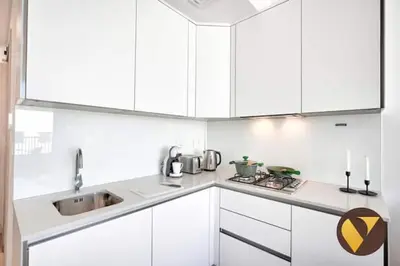 a white kitchen with white cabinets and a sink at Vogue JVC Luma22 near Circle Mall, Studio Apartment with Balcony and Vibrant Community View, Access to all Amenities in Dubai