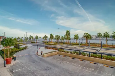 a parking lot with palm trees and a body of water at Port De La Mer by Hosteeva in Dubai