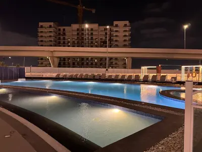 a large swimming pool with chairs in a city at night at Smart Studio in Gemz in Dubai