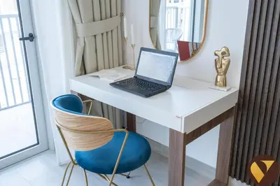 a laptop computer sitting on a white desk with a blue chair at Vogue JVC Luma22 near Circle Mall, Studio Apartment with Balcony and Vibrant Community View, Access to all Amenities in Dubai