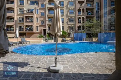a swimming pool with an umbrella and a large building at Peaceful 1BR JVC Near Circle Mall Pool Gym in Dubai