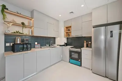 a kitchen with white cabinets and a stainless steel refrigerator at Golden Stays - Italian Riviera 4BR Villa I Stylish Bliss Living in Dubai
