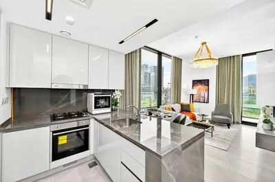 a kitchen with white cabinets and a living room at Golden Stays - Luxe 1BR Retreat I Cinema Access & Elegant Stay in Dubai