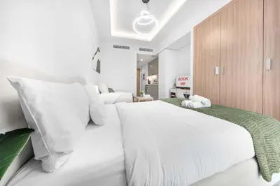 a white bedroom with two beds and a cabinet at StayShort - Studio Apartment at Azizi Riviera with Balcony in Dubai