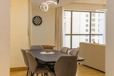 a dining room with a table and chairs and a clock at 2BR Beach Side Lux JBR Retreat - Luxury Pool Bahar in Dubai