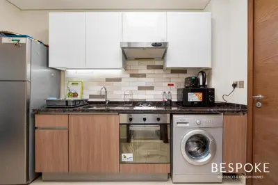 a kitchen with white cabinets and a washing machine at Bespoke Holiday Homes - Cozy Modern Studio in Samia by Azizi in Dubai
