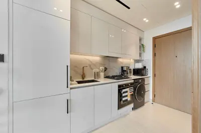 a kitchen with white cabinets and a washer and dryer at Modern Studio at Binghatti Azure In Heart of JVC in Dubai