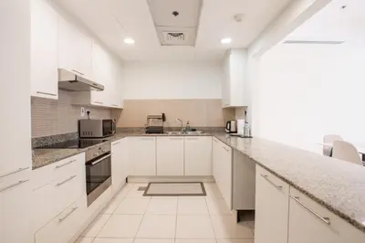 a white kitchen with white cabinets and granite counter tops at Nivis find- Bay square -1 BHK in Dubai