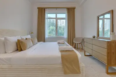 a white bedroom with a large bed and a dresser at Al Sarrood, Palm Jumeirah - 1 Bedroom Apartment - Allsopp & Allsopp in Dubai