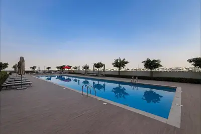 a large swimming pool with tables and umbrellas on a building at Cozy 2BR Apartment in Dubai Hills with Cinema and Lounge Access in Dubai