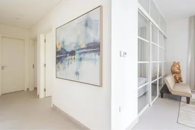 a white hallway with a painting on the wall and a chair at Cozy 2BR Apartment in Dubai Hills with Cinema and Lounge Access in Dubai