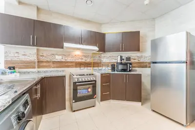 a kitchen with wooden cabinets and a stainless steel refrigerator at Community View 1BR, Perfect Location Near Miracle Garden, Butterfly Garden and Community Spaces, Orion Building, Arjan by Deluxe Holiday Homes in Dubai