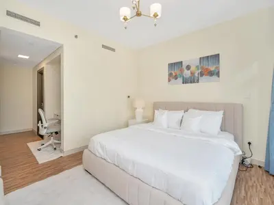 a white bedroom with a large bed and a bathroom at 2BR Panoramic City - Burj and Fountain View in Dubai