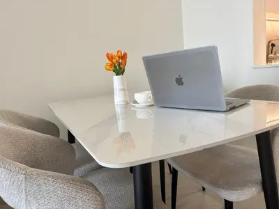 a white table with a laptop and a vase with flowers at Modern & Cozy 1BR Apartment with Full Comfort in Dubai