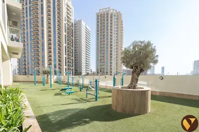 a playground with a tree in a park with tall buildings at Vogue JVC Jeewar Tower Near Circle Mall, One Bedroom Apartment with Balcony and City View, Access to all Amenities in Dubai