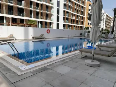 a swimming pool with two chairs and an umbrella at Large 1 Bedroom Apartment in Azizi Riviera 15 in Dubai