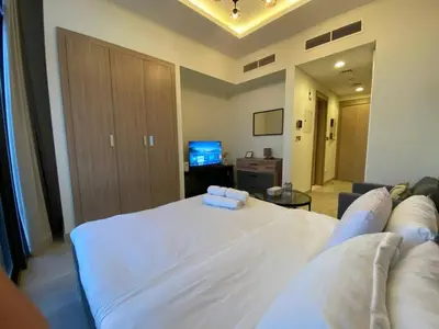 a bedroom with a large white bed and a living room at Modern Studio in Azizi Riviera 10, Near Downtown in Dubai