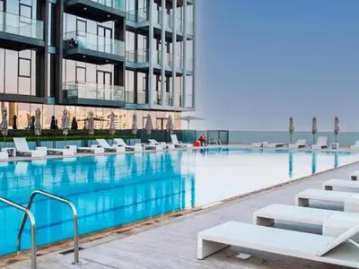 a swimming pool with white chairs in front of a building at Stylish & Peaceful 2BR Home in JVC District in Dubai
