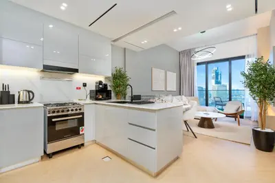 a kitchen with white cabinets and a living room at Stylish 1BR Canal & Burj View High Floor in Dubai