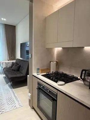 a kitchen with a stove and a living room at Stylish Studio JVC I Epic Amenities I Near Mall in Dubai