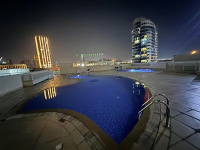 a large swimming pool in a city at night at Cozy Studio Apartment in JCV in Dubai