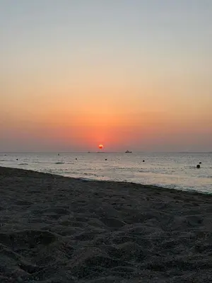 a beach with the sun setting in the ocean at La Mer Iconic View 1 bedroom in Dubai