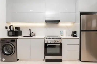 a white kitchen with a stove and a refrigerator at GuestReady - Studio l Partial Burj Khalifa View in Dubai