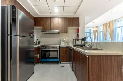 a kitchen with a stainless steel refrigerator and wooden cabinets at Cozy 2BR Near Zabeel Park - Dubai frame view in Dubai