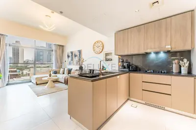 a kitchen with brown cabinets and a living room at Community View 1BR, Just 15minutes to Miracle Garden - Oxford Boulevard, Jumeirah Village Circle by Deluxe Holiday Homes in Dubai